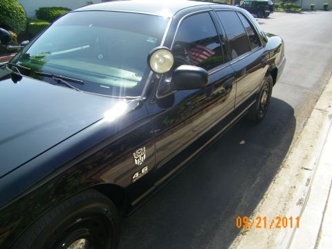 2003 Ford Crown Victoria - Side view of black Ford with 4.6 fender emblem, side mirror and small American flag visible inside