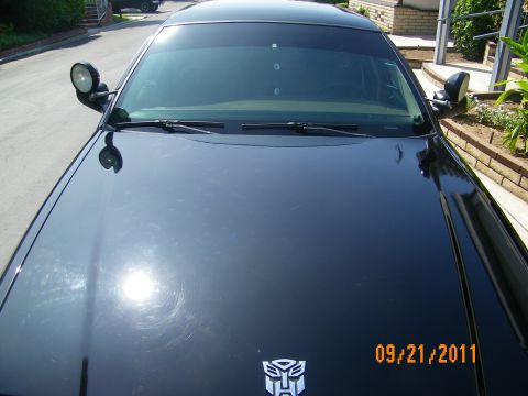 2003 Ford Crown Victoria - Front hood of glossy black car showing wipers, mirrors and an Autobot symbol decal at the hood tip