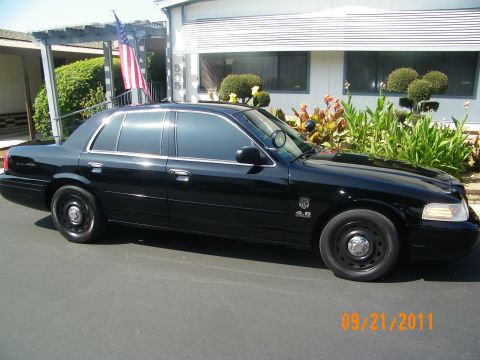 2003 Ford Crown Victoria - Glossy black sedan angled toward camera showing front grille, headlights and emblem on front door