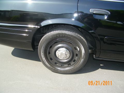 2003 Ford Crown Victoria - Detail of rear wheel and fender on black car, Firestone branding visible on tire sidewall