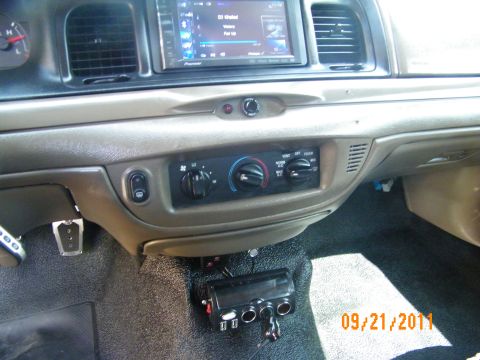 2003 Ford Crown Victoria - Tan vehicle center stack showing HVAC knobs, headlight switch and a screen above, device on carpet