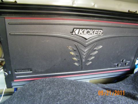 2003 Ford Crown Victoria - Close-up of a dusty Kicker amplifier face showing gain and crossover control ports.