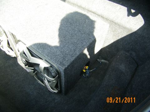 2003 Ford Crown Victoria - Single-sub carpeted enclosure sitting in a trunk, wiring loom exposed beside it.
