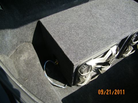 2003 Ford Crown Victoria - Dual-driver subwoofer box with white cones tucked into a carpeted trunk corner.