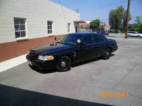2003 Ford Crown Victoria - Blacked-out Crown Victoria with steel wheels and a driver spotlight on a paved lot.