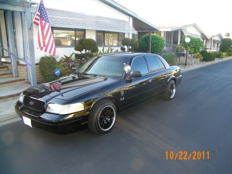 2003 Ford Crown Victoria - Lowered black Crown Victoria on dark multi-spoke wheels in front of a flag-flying house.