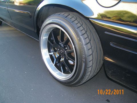 2003 Ford Crown Victoria - Dark multi-spoke wheel wrapped in a Dunlop tire mounted on a black sedan rear.