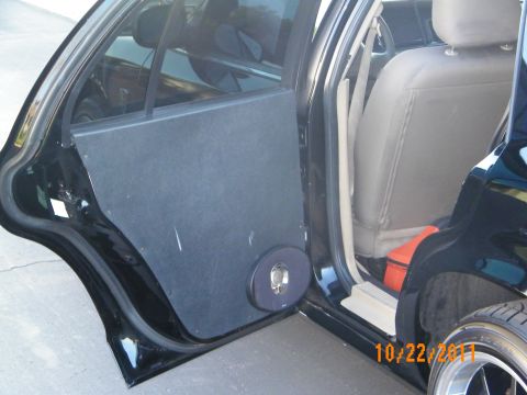 2003 Ford Crown Victoria - Rear door fitted with a fabric-wrapped audio panel beside tan seats and a wheel