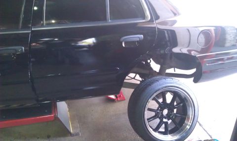 2003 Ford Crown Victoria - Rear corner of a black sedan on a lift with a swapped black wheel alongside
