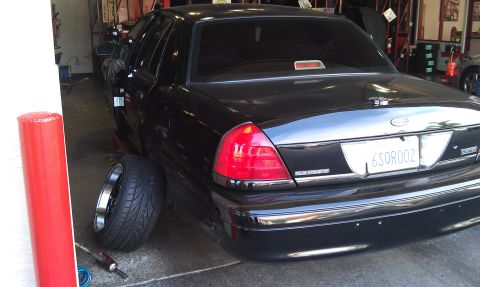 2003 Ford Crown Victoria - Black Crown Victoria seen from behind in a service bay with a spare wheel nearby