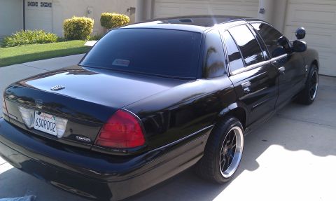 2003 Ford Crown Victoria - Rear quarter of a black Crown Victoria on a driveway, trunk badge and black wheels visible