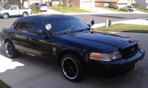 2003 Ford Crown Victoria - Crown Victoria with A-pillar spotlight parked on a driveway, trucks and homes in background