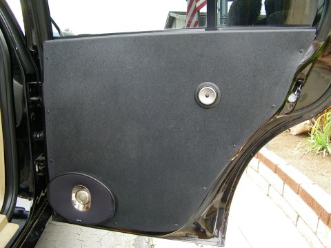 2003 Ford Crown Victoria - Open rear door of a black sedan showing a carpeted panel with two flush-mounted speakers