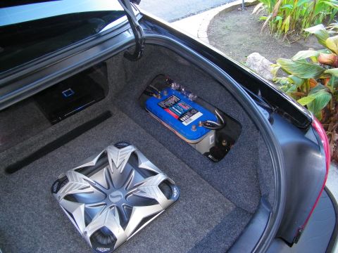 2003 Ford Crown Victoria - One Kicker sub beside a blue battery in a sedan trunk with foliage visible outside