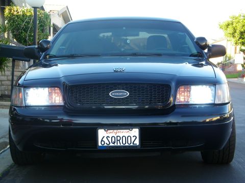2003 Ford Crown Victoria - Head-on view of a black Crown Victoria Interceptor with grille badge and lit headlamps