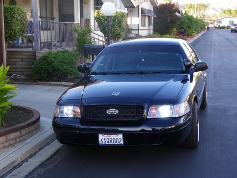 2003 Ford Crown Victoria - Three-quarter front view of a black Crown Victoria at the curb with headlamps lit