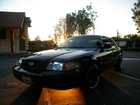2003 Ford Crown Victoria - Black Crown Victoria parked in a lot at sunset, headlights on, dark wheels