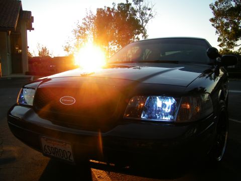 2003 Ford Crown Victoria - Sun flare across the hood of a black Crown Victoria with lit headlamp and grille badge