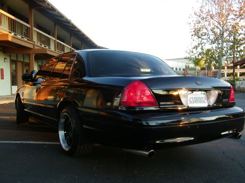 2003 Ford Crown Victoria - Murdered-out Crown Victoria viewed from rear, dual exhaust tips and tinted taillights, parked outside a motel building.