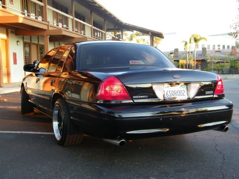 2003 Ford Crown Victoria - Rear of a blacked-out Ford Crown Victoria at dusk, dual chrome exhaust tips, palm trees behind.