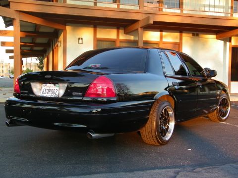 2003 Ford Crown Victoria - Crown Victoria sedan shot from passenger rear, wood-beam motel facade in golden light.