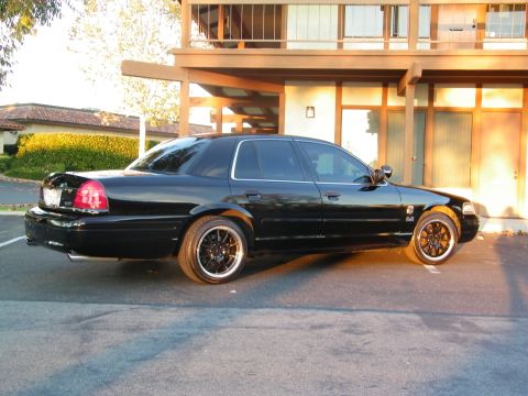 2003 Ford Crown Victoria - Side rear angle of a black Crown Victoria in a parking lot, two-story stucco building behind.