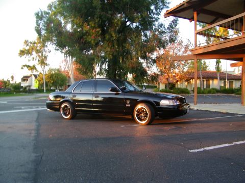 2003 Ford Crown Victoria - Black Crown Victoria angled toward camera in a parking lot, school-crossing sign in background.