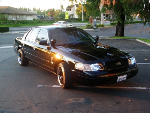 2003 Ford Crown Victoria - Black Crown Victoria with custom dark grille and lit headlights, parked outside an office.