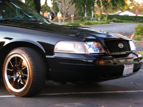 2003 Ford Crown Victoria - Tight front-corner shot of a black Crown Victoria, black bronze-lip wheel and lit headlight.