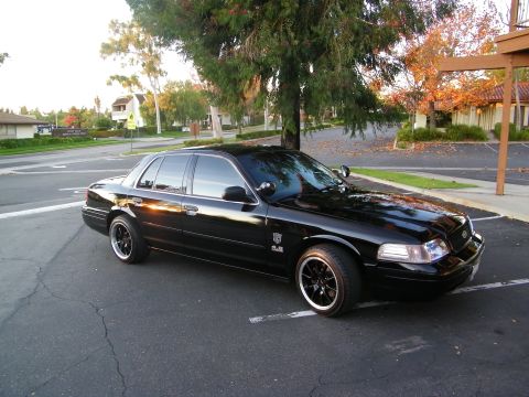 2003 Ford Crown Victoria - Glossy black Crown Victoria angled toward camera, badge on fender and black wheels.