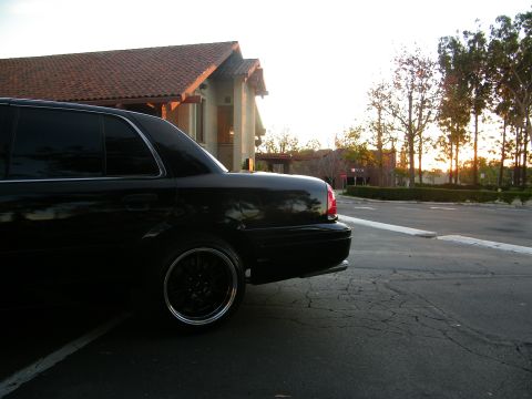 2003 Ford Crown Victoria - Low rear-corner shot of a black Crown Victoria, black lip wheel and tiled-roof building behind.