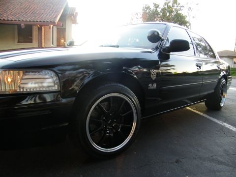 2003 Ford Crown Victoria - Low front-corner view of a black Crown Victoria with clear headlights and a 4.6 fender emblem.