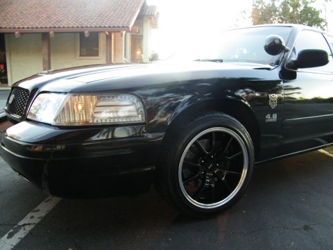 2003 Ford Crown Victoria - Tight front-quarter shot of a black Crown Victoria, glossy fender and black lip wheel.