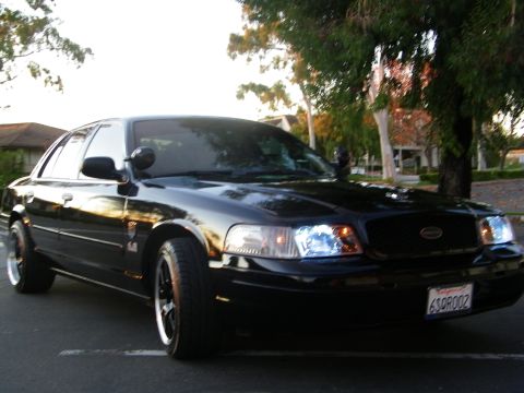 2003 Ford Crown Victoria - Driver-side front quarter of a lowered black Ford sedan parked along a curb at dusk.