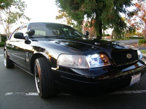 2003 Ford Crown Victoria - Tight close-up on the front fender, headlight and grille of a black Ford sedan.