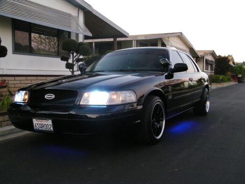 2003 Ford Crown Victoria - Driver-side front quarter of a black Ford sedan glowing blue underneath at twilight.