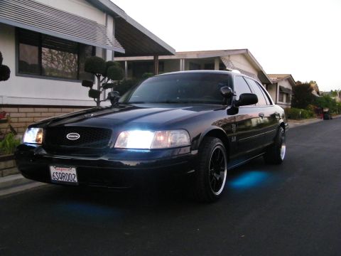 2003 Ford Crown Victoria - Black Ford sedan showing cyan underglow parked in front of a single-story home.