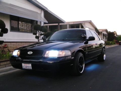 2003 Ford Crown Victoria - Driver-side front quarter of a black Ford sedan parked curbside at dusk.