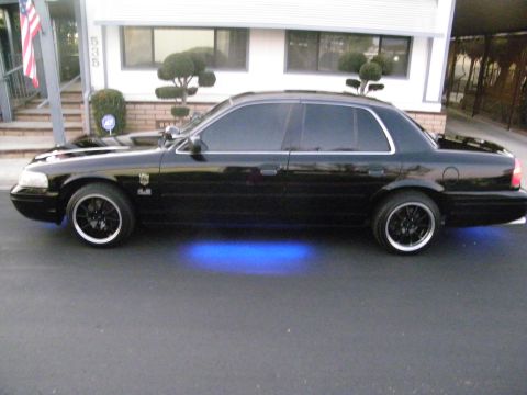 2003 Ford Crown Victoria - Side profile of a black Ford sedan on black wheels with blue underglow near a building.
