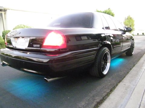 2003 Ford Crown Victoria - Rear-quarter shot of a black Ford sedan with cyan underglow and lit taillights.