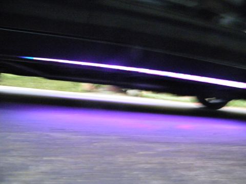 2003 Ford Crown Victoria - Purple underglow lighting casts a glow under a black vehicle's rocker panel against dark asphalt.
