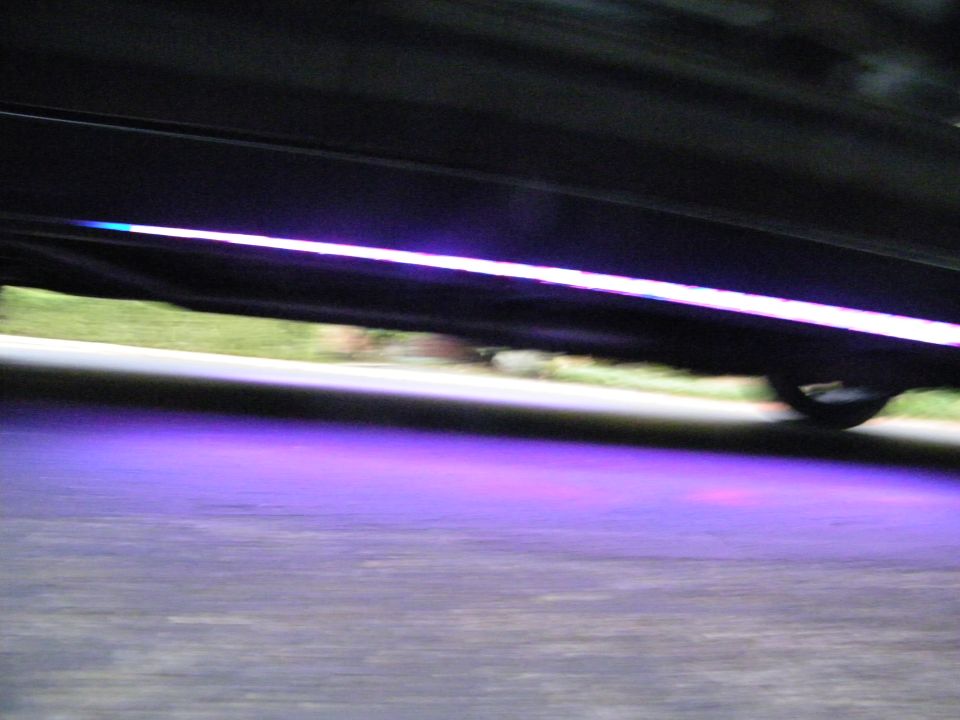Underbody of black car with purple LED underglow on pavement, motion-blurred rocker panel