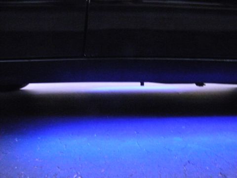 2003 Ford Crown Victoria - Blue underglow lighting spills onto the road beneath a black vehicle's lower body panel.