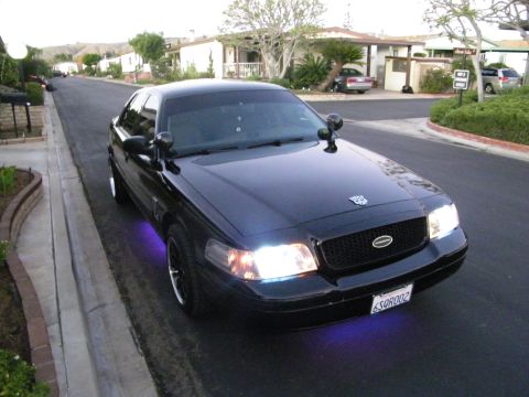 2003 Ford Crown Victoria - Elevated front view of a black Ford full-size sedan with purple underglow and lit headlights on a street.