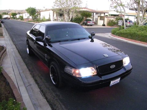 2003 Ford Crown Victoria - Black Ford sedan with oval Ford emblem and bright headlights photographed from the front corner.