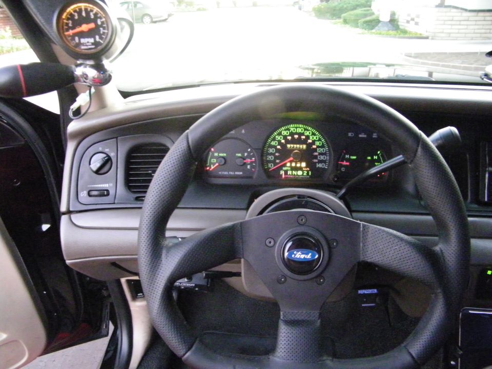 Ford car interior dash with aftermarket steering wheel, digital cluster, and A-pillar tachometer