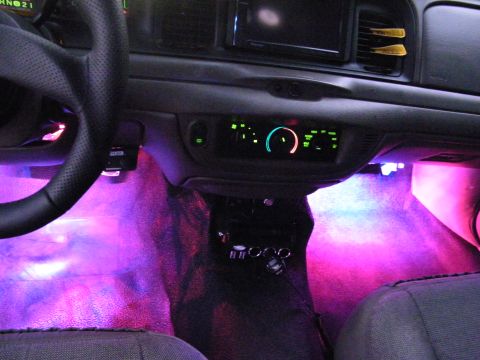 2003 Ford Crown Victoria - Interior of a Ford sedan with pink-purple footwell LEDs, glowing climate controls and cloth seating.