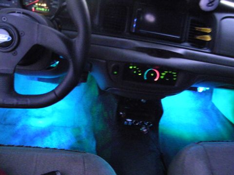 2003 Ford Crown Victoria - Teal-blue LED footwell lighting in a Ford interior with illuminated gauges and cloth bucket seats.