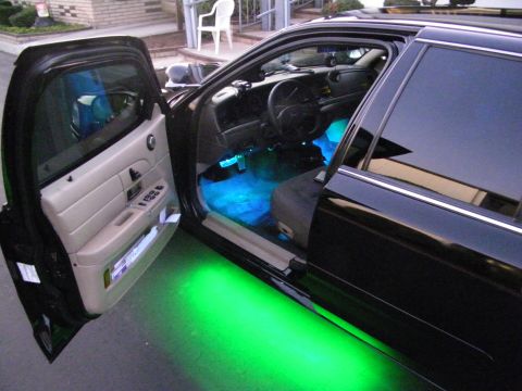 2003 Ford Crown Victoria - Black Ford sedan, door open, showing blue cabin lighting and green underglow on the pavement.