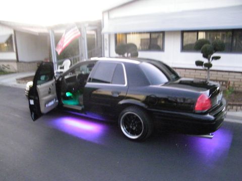 2003 Ford Crown Victoria - Side view of black full-size sedan with purple underbody lights, tan interior visible through open door